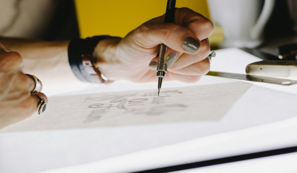 person lettering on tracing paper using mechanical pencil